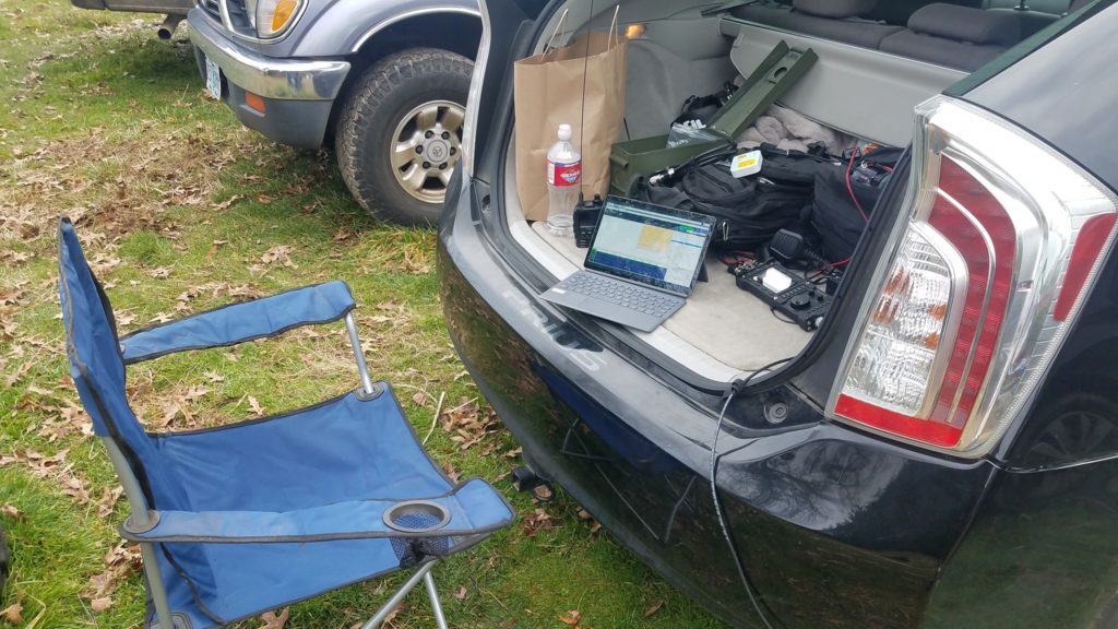 Picture of radio equipment in the back of a Prius along with a folding chair facing the hatch back.