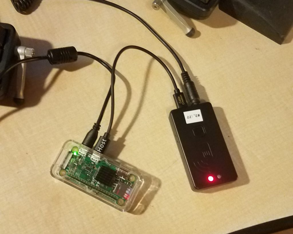 A Raspberry Pi W Zero in a clear acrylic case connected to a Mobilinkd TNC3 with a MicroUSB OTG cable, host end connected to the Pi's USB OTG port.