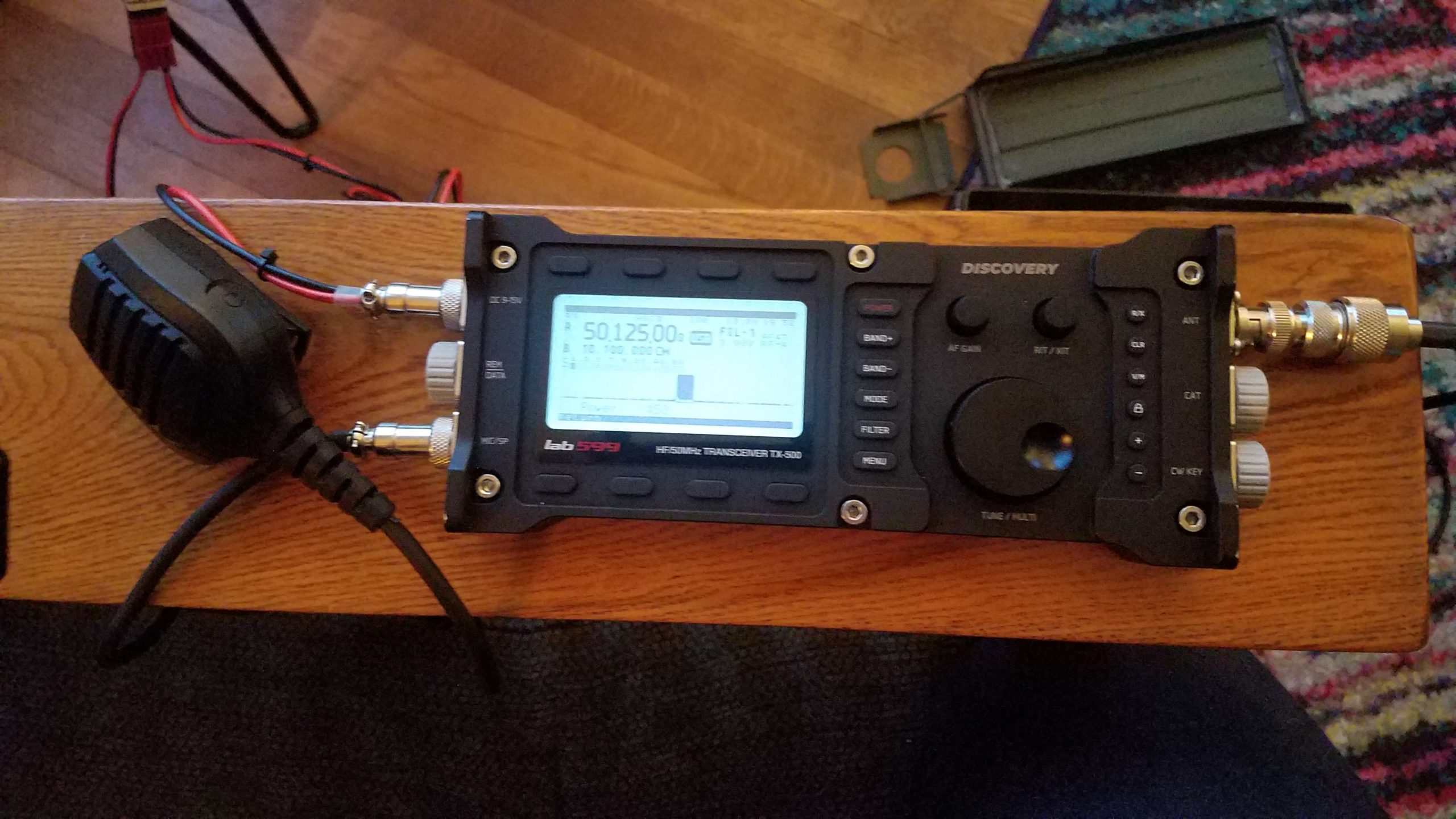 Lab599 TX-500 radio powered up and tuned to 50.125 MHz sitting on a chair arm along a microphone.