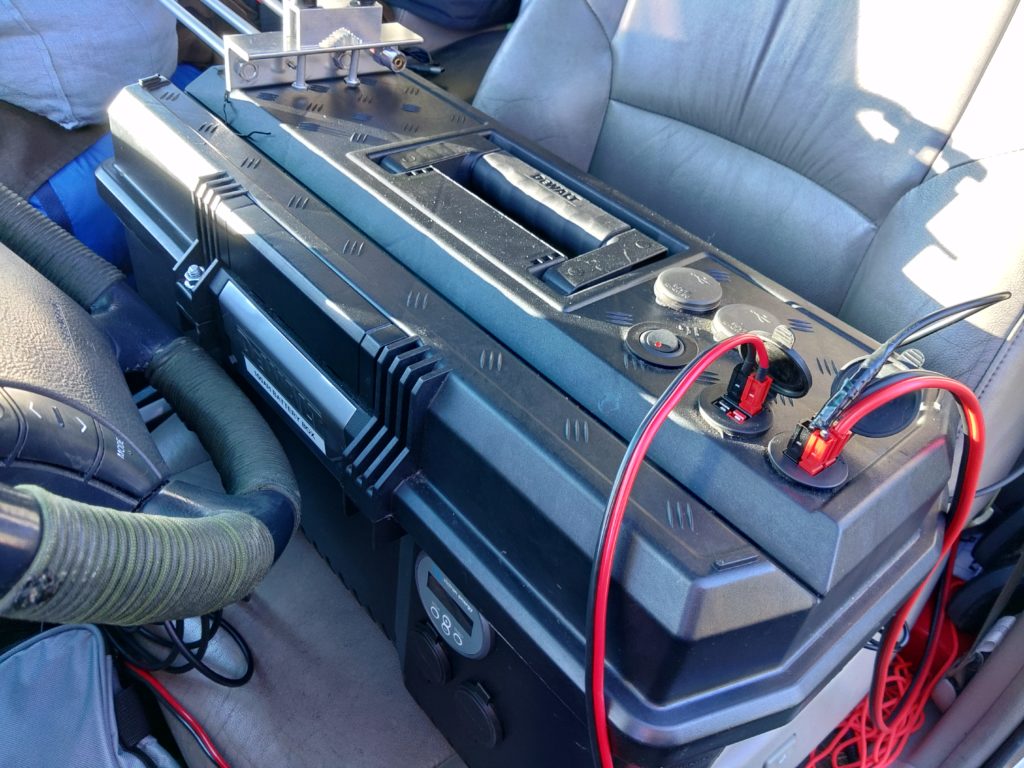 A toolbox with power connections running from it sitting in the front seat of a vehicle.