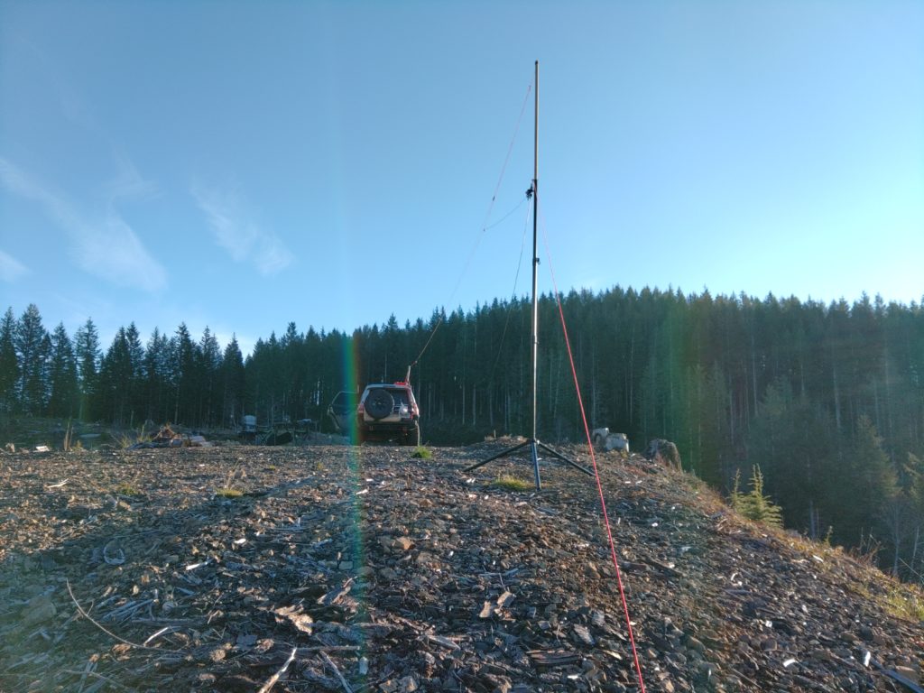 View of an antenna mast guyed to the ground and a line with an antenna running to a SUV in the background